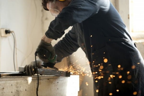 Skilled workman grinding metal pipe with a lot of sparks